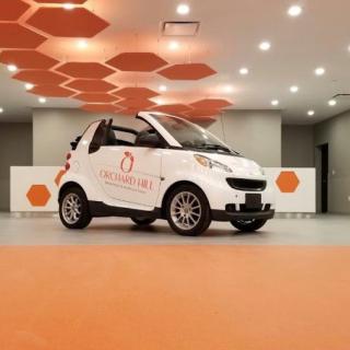 A white Smart car displayed in a modern, orange-themed indoor setting.