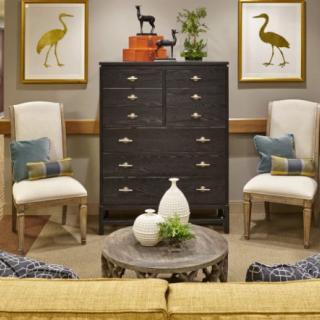 A cozy living room featuring a black dresser, two elegant chairs, and colorful artwork on the walls.