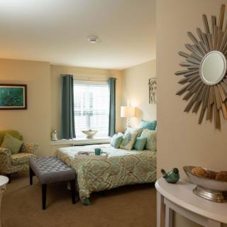 A cozy bedroom with tasteful decor, featuring a bed, chair, and stylish mirror.