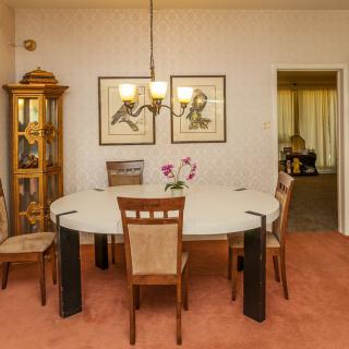 A cozy dining room with a round table, surrounded by chairs, illuminated by a chandelier, and adorned with wall art and a glass cabinet.