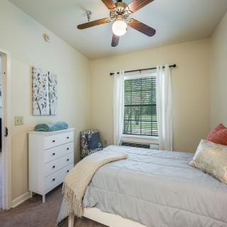 A cozy bedroom with a bed, dresser, and ceiling fan, featuring a window with a view.