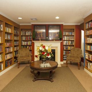 A cozy library with bookshelves lining the walls, a central fireplace, and comfortable seating.