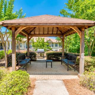 A peaceful gazebo surrounded by lush greenery and benches, providing a relaxing outdoor setting on a sunny day.