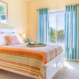 A bright and cozy bedroom with colorful striped bedding and light blue curtains.