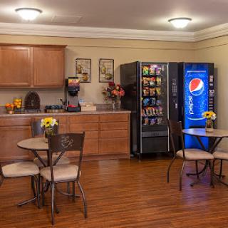 A cozy breakroom featuring a vending machine with Pepsi and snacks, complemented by tables and chairs for relaxation.