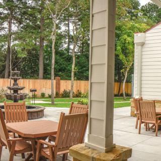 A serene outdoor patio with wooden furniture and a fountain, surrounded by lush landscaping.