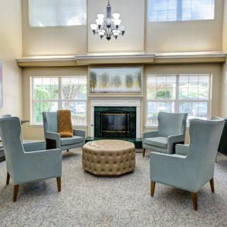A cozy living room with armchairs arranged around a central ottoman, a fireplace, and large windows allowing natural light to flood the space.