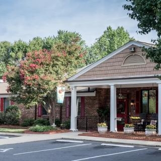 A quaint building with a welcoming entrance surrounded by trees and a parking lot.