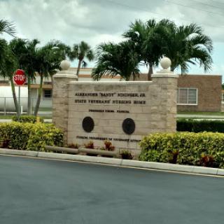 Entrance sign to a community facility surrounded by palm trees.