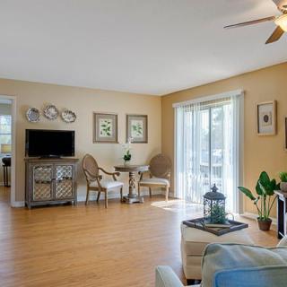 A cozy living room with wooden flooring, featuring a TV, seating area, and plenty of natural light.