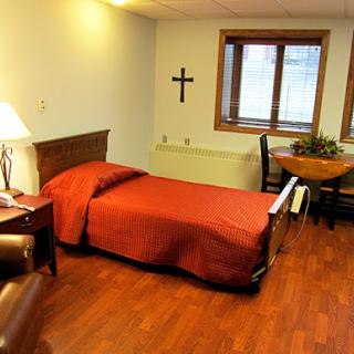 A cozy bedroom featuring a single bed with red bedding, wooden furniture, and a warm ambiance.