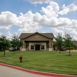 A small building with a well-maintained lawn and trees under a partly cloudy sky.
