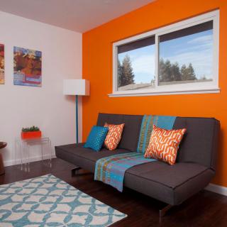 A modern living room with an orange accent wall and a gray sofa adorned with colorful pillows.
