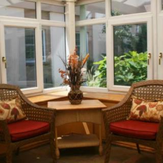A cozy conservatory with wicker chairs and a table, surrounded by large windows letting in natural light.