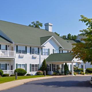 A two-story residential building with a green roof and surrounding trees.