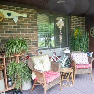 A cozy porch with wicker chairs, vibrant plants, and charming decor against a brick wall.