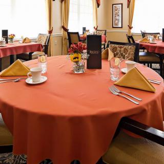 A neatly set dining table in a restaurant with orange tablecloths and folded napkins.