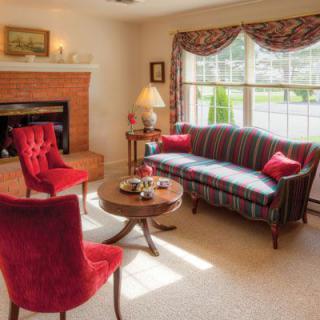 A cozy living room with traditional decor, featuring red chairs, a striped sofa, and a fireplace.