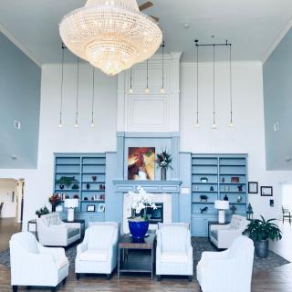 A spacious and elegantly designed living room featuring a grand chandelier, comfortable seating area, built-in bookshelves, and a stylish fireplace with blue and white decor accents.