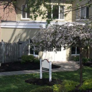 A residential building with a garden, featuring a blooming tree and an empty signpost.