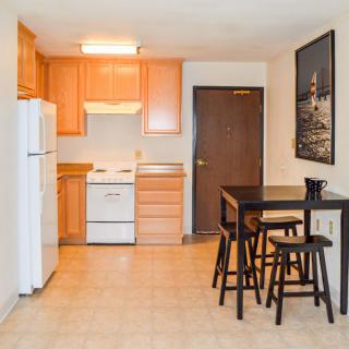 A compact apartment kitchen with wooden cabinets and a small dining area featuring a table and stools.