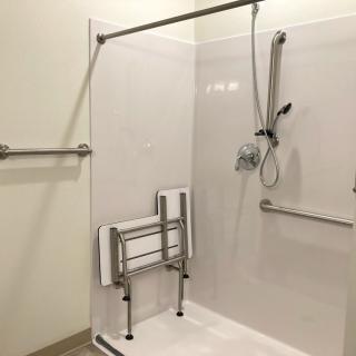 An accessible shower with handrails and a folding seat for support.