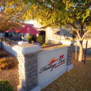 A cozy restaurant with outdoor patio seating shaded by trees, featuring a prominent sign at the entrance.