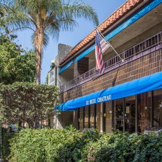 An outdoor view of a building featuring a blue awning and an American flag, surrounded by lush greenery and palm trees.