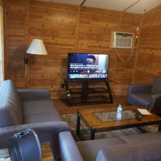 A cozy living room with wooden walls, featuring sofas, a television, and an air conditioner.