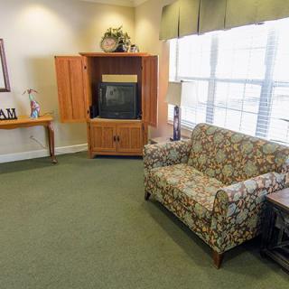 A cozy living room featuring a patterned couch, a wooden TV cabinet, and large windows with natural lighting.