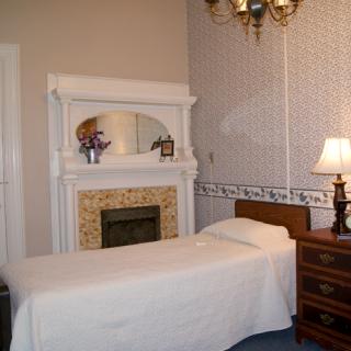 A classic bedroom with a single bed, ornate fireplace, and a lamp on the nightstand.