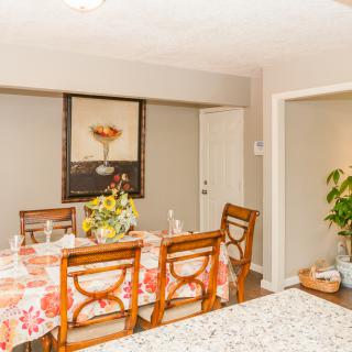 A beautifully decorated dining room with a floral tablecloth, elegant chairs, and artwork on the wall.