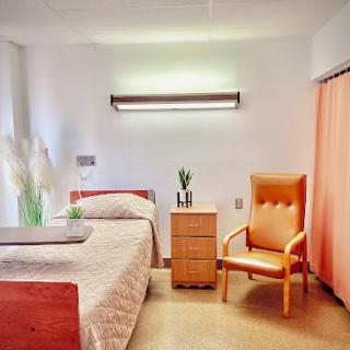 A well-lit and minimalistic hospital room featuring a bed, a chair, and a nightstand.