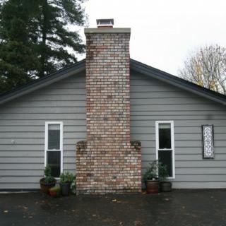 A house exterior with a central brick chimney and two windows on either side.