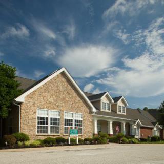 A suburban brick house with a well-maintained lawn and driveway under a partly cloudy sky.