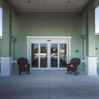 A building entrance with sliding glass doors and two chairs on the patio.