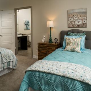 A cozy bedroom with two twin beds featuring turquoise bedding and a nightstand with a lamp.