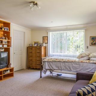 A cozy bedroom with a bed, dresser, television, and shelves on a sunny day.