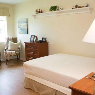A cozy bedroom with a neatly made bed, wooden dresser, and a chair by the window.