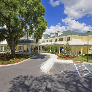 The entrance of a hospital building with a landscaped parking lot and trees.