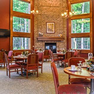 A cozy restaurant dining area with a brick fireplace and large windows offering a view of the surrounding forest.