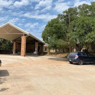 A view of a building with a covered area and parked cars, surrounded by trees under a partly cloudy sky.