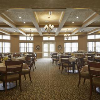 An elegant dining room with neatly arranged tables and chairs, featuring large windows and warm lighting.