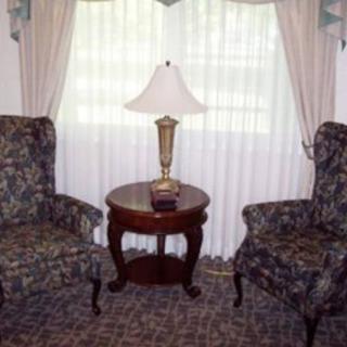 A cozy sitting area with two patterned chairs, a round wooden table, and a lamp by the window.