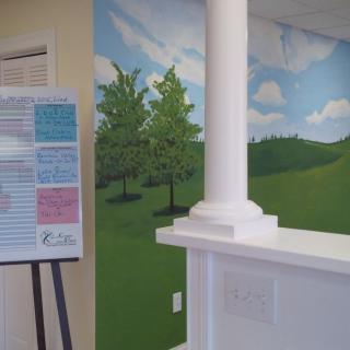 A reception area with a mural depicting trees and clouds, alongside a column and an informational poster.