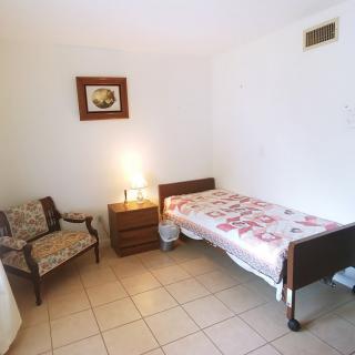 A minimalist bedroom with a single bed, chair, dresser, and a lamp.