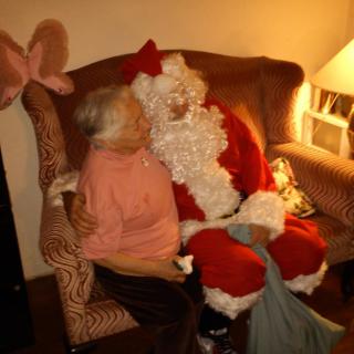 An elderly person sitting on a sofa with Santa Claus during the holiday season.