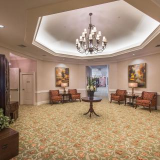 A well-appointed lobby featuring a chandelier, comfortable seating, decorative paintings, and a table with flowers.