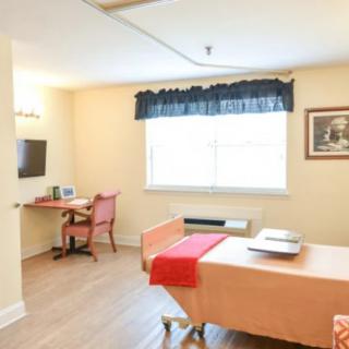 A well-lit room with a bed, desk, and television.