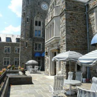 A stone building with a clock tower, featuring outdoor seating with tables and striped umbrellas.